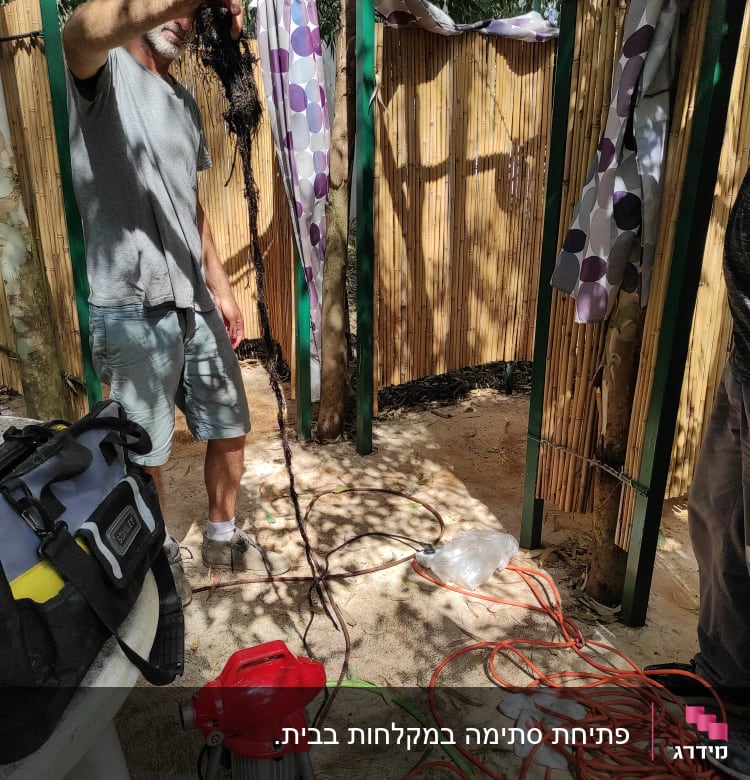 אדם מחזיק שורש סתום, כלי עבודה וצינור על הרצפה